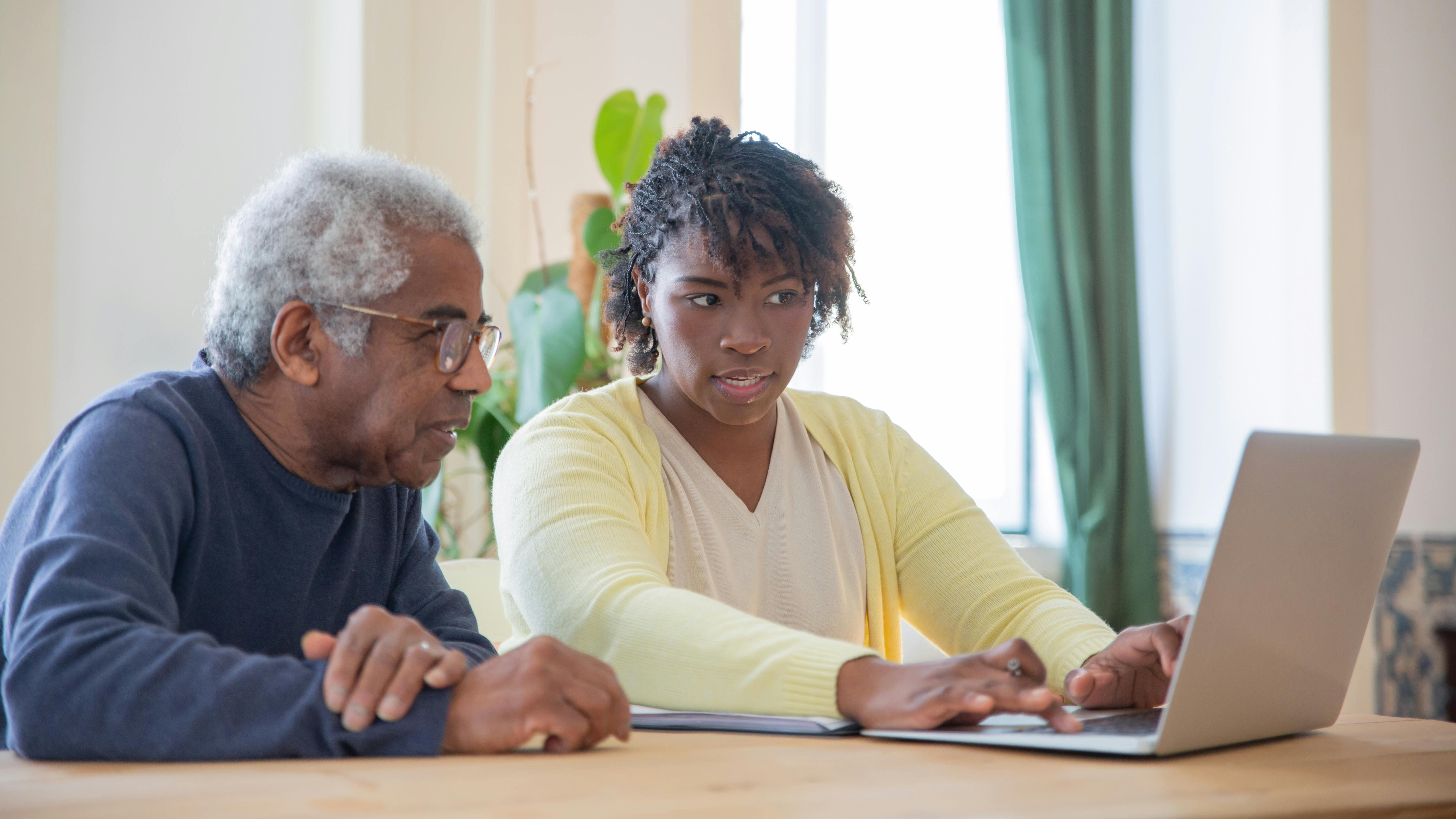 A man and a woman look at a laptop while talking to each other.